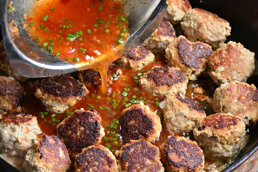 pouring chili sauce over cooked meat balls in a cast iron skillet 