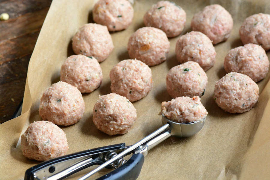 using a cookie scoop to make even meatballs which are on a baking sheet lined with butcher paper with the cookie scoop 