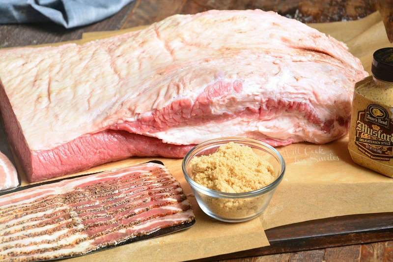 brisket and ingredients to make the brisket bacon, brown sugar, and mustard on parchment paper on a wood cutting board 