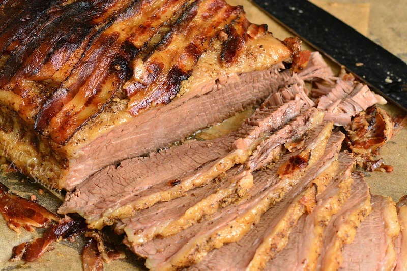 beef brisket sliced on parchment paper on top of a wood cutting board with a knife 