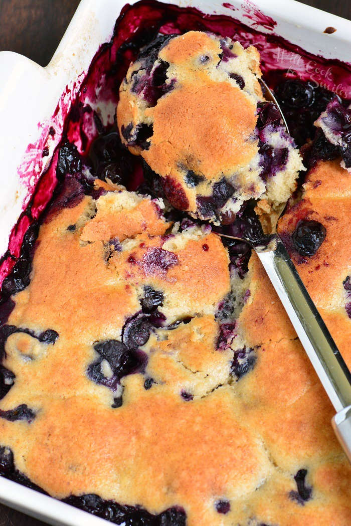 easy blueberry cobbler in a casserole dish being scooped out by a metal serving spoon 