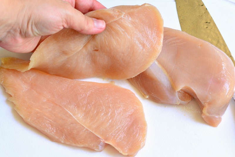 cutting raw chicken width-wise on a cutting board 
