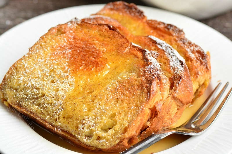 french toast in the oven on a plate with syrup on it with a fork on a wood table 