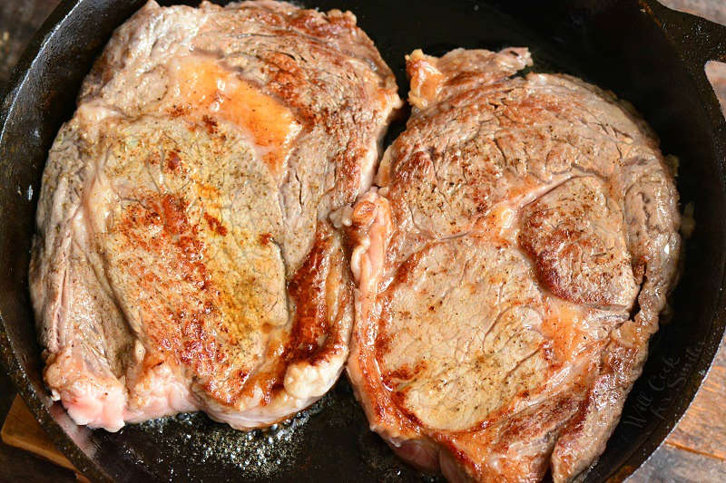 two rib eye steaks searing in the cast iron skillet. 