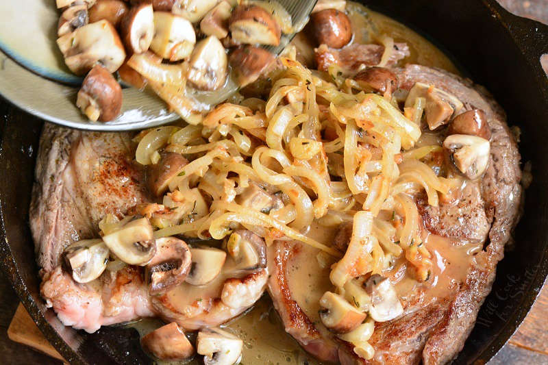 topping steaks with mushrooms and onions in a cast iron skillet 