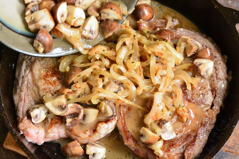 adding mushrooms and onions to the steaks in the skillet.