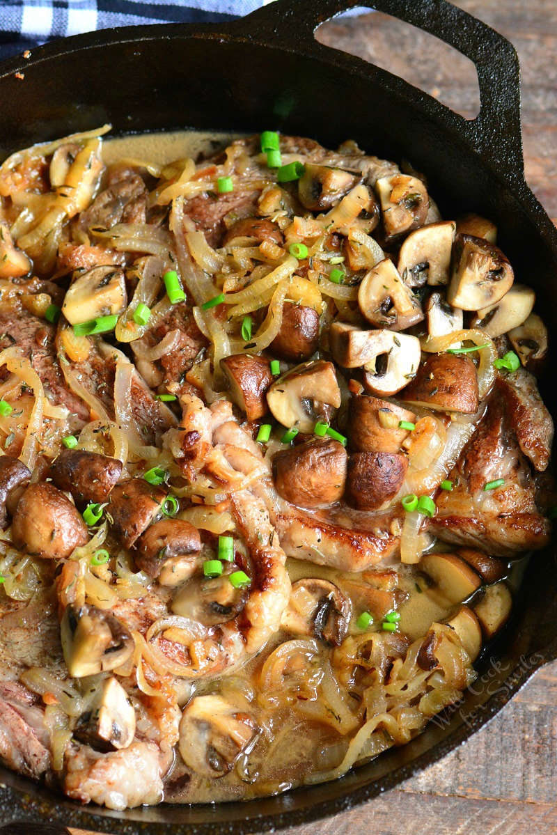 Rib Eye Steaks in mushrooms and onions in a cast iron skillet 