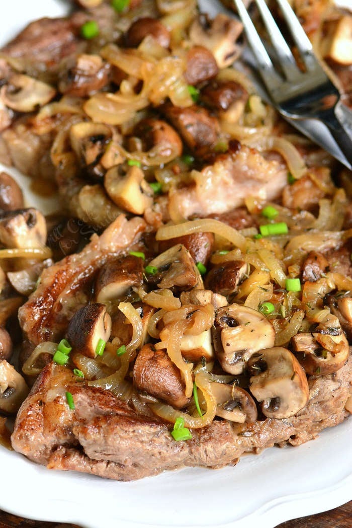 rib eye steaks topped with mushrooms and onions on a plate with a fork 