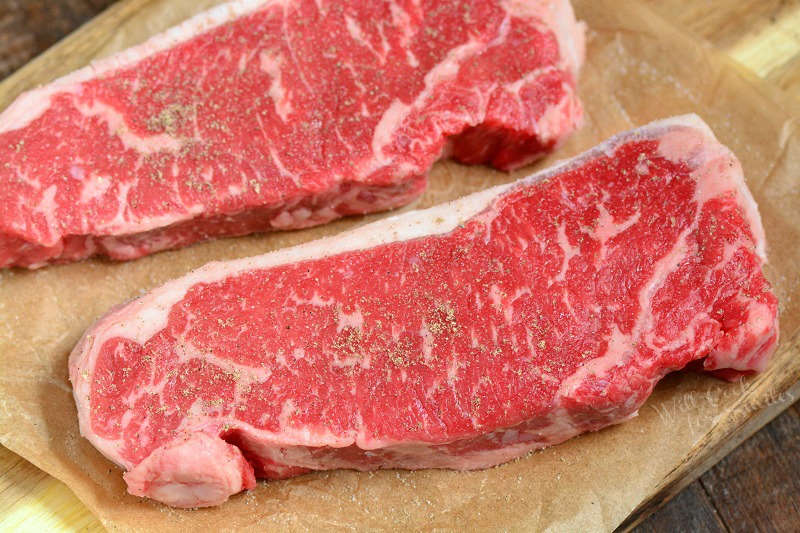 raw strip steaks on parchment paper