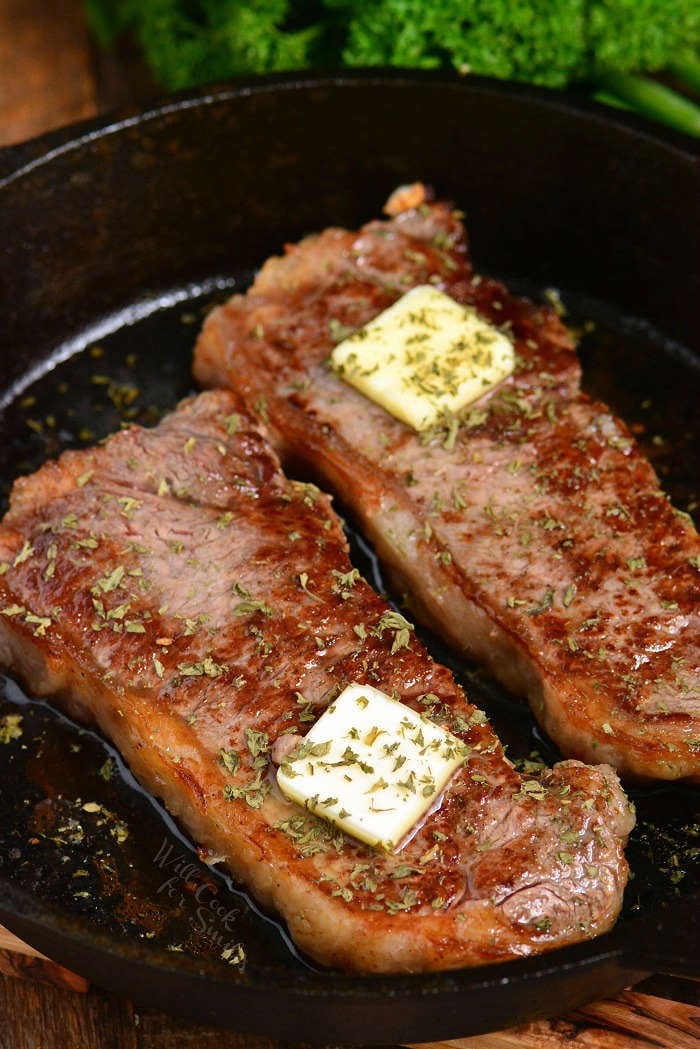 two sirloin steaks topped with butter square and herbs on a cast iron skillet