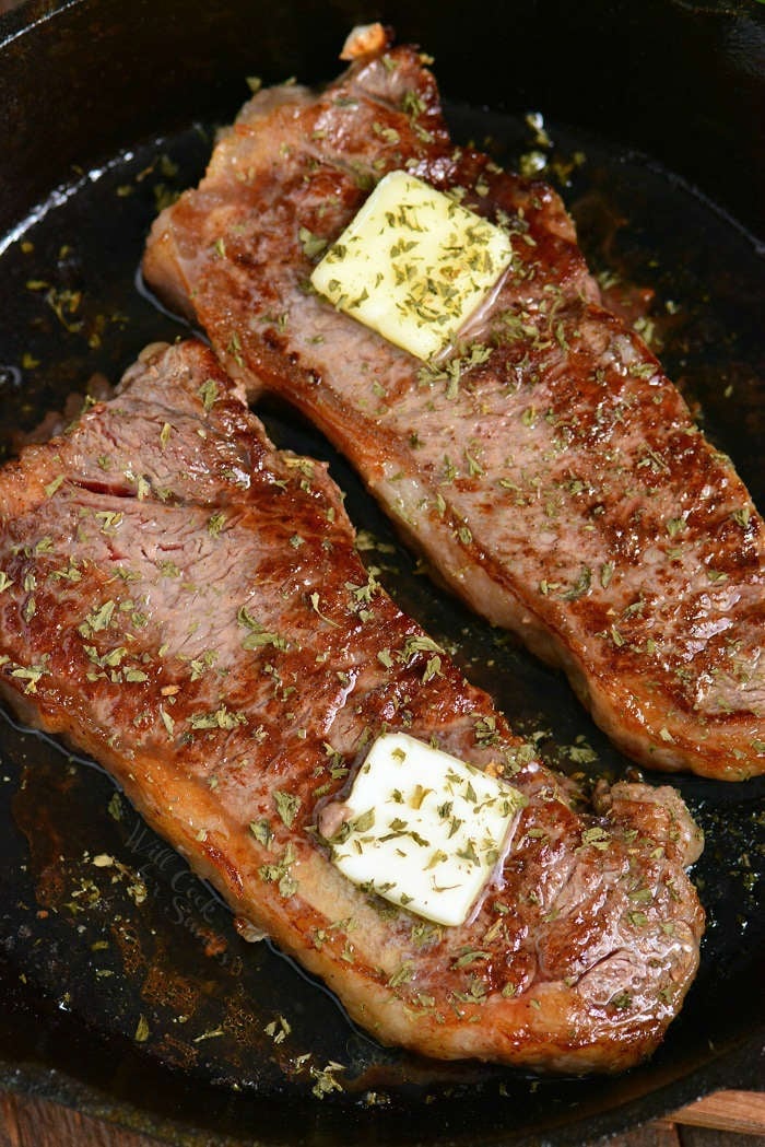 closer view of steaks in the skillet topped with butter squares and herbs