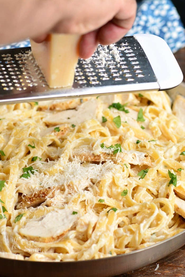 grating cheese over chicken alfredo with fettuccine in a pan