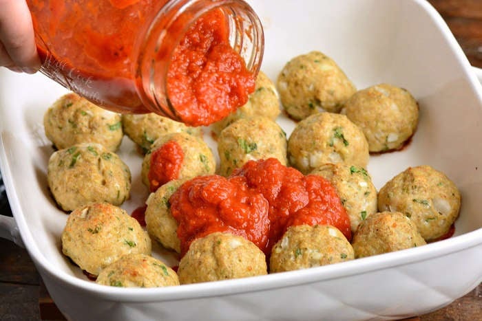 pouring sauce over cooked chicken meatballs in a baking dish