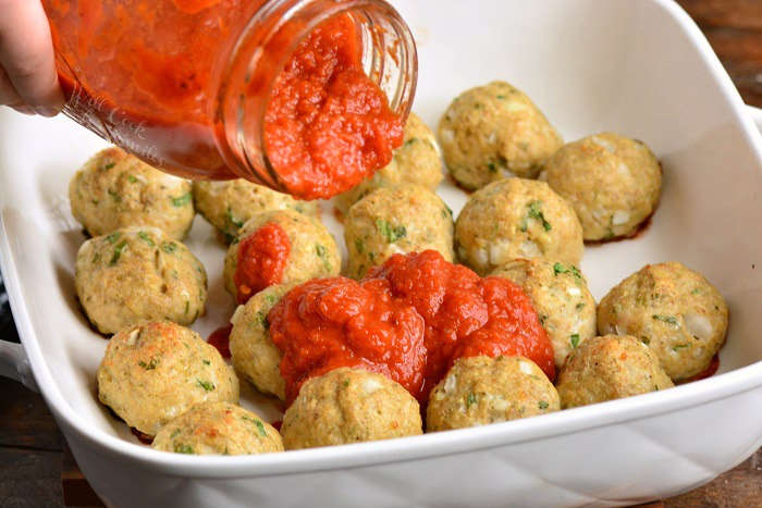 pouring sauce over cooked chicken meatballs in a baking dish