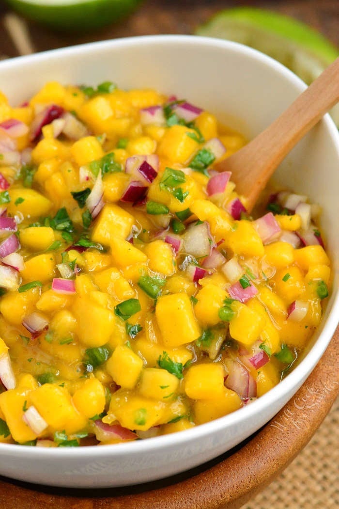 Mixed mango salsa in a white bowl with a wooden spoon.