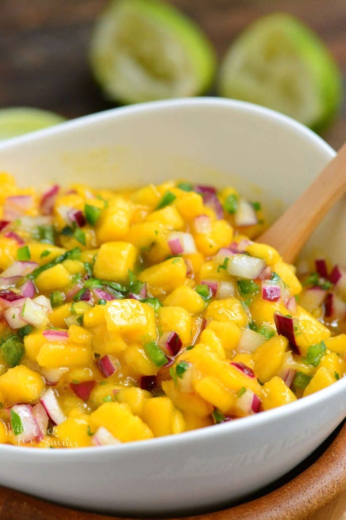 Mango salsa in a white bowl with a spoon and squeezed in the background.