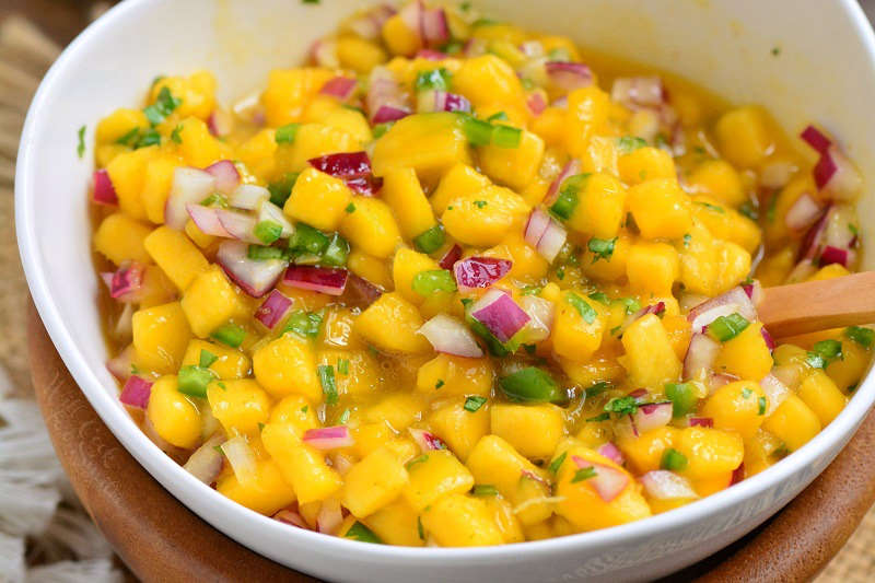 mango salsa in a white bowl in a wooden with a spoon. 