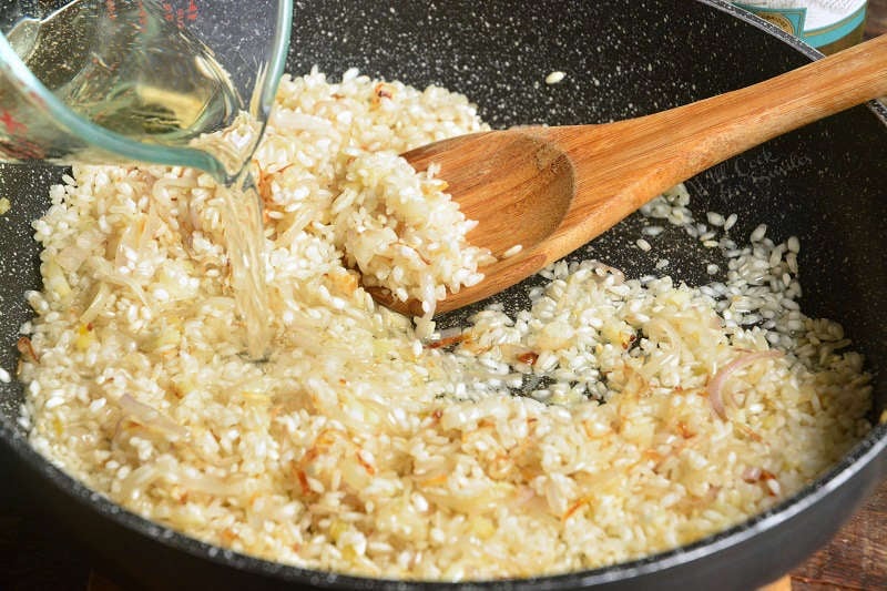 adding liquid to the risotto that is in a pan with a wooden spoon 