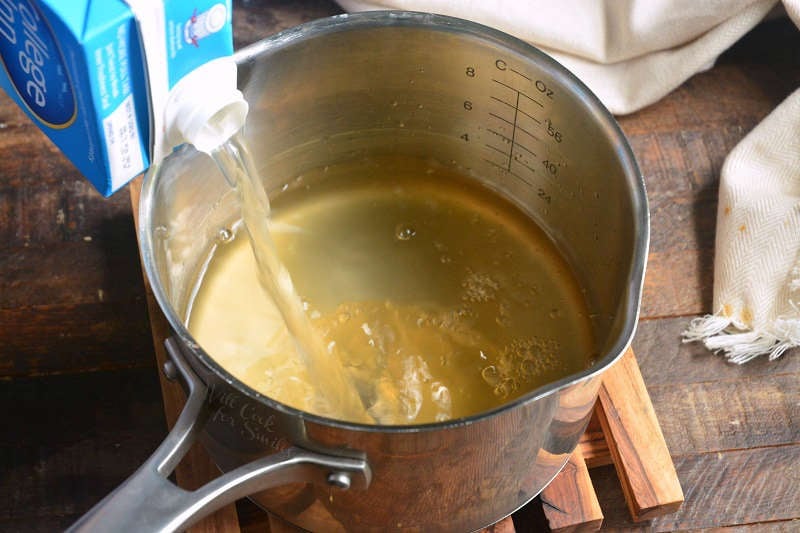 Chicken broth being poured into a pot that is sitting on a wood table 