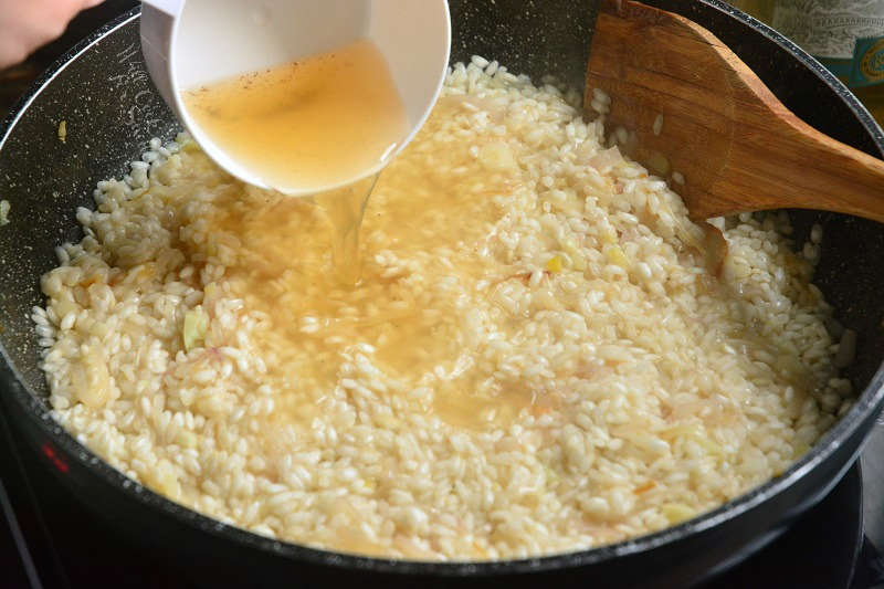 adding broth to risotto that is in a pan with a wooden spoon 