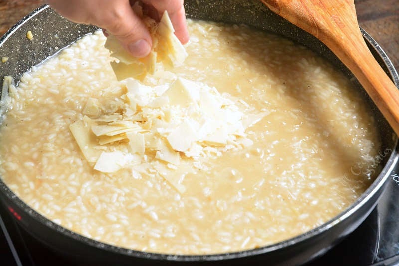 adding Parmesan cheese a couple of minutes before risotto is ready into a pan with a wooden spoon 