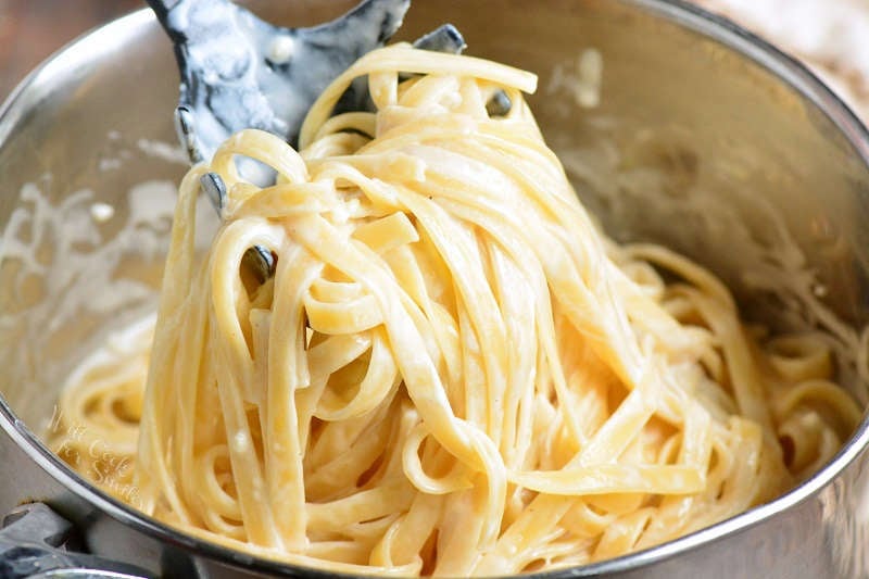 fettuccine Alfredo in a pot being picked up by a plastic spoon 