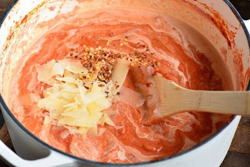 ingredients in vodka sauce being mixed in a stock pot with a wooden spoon