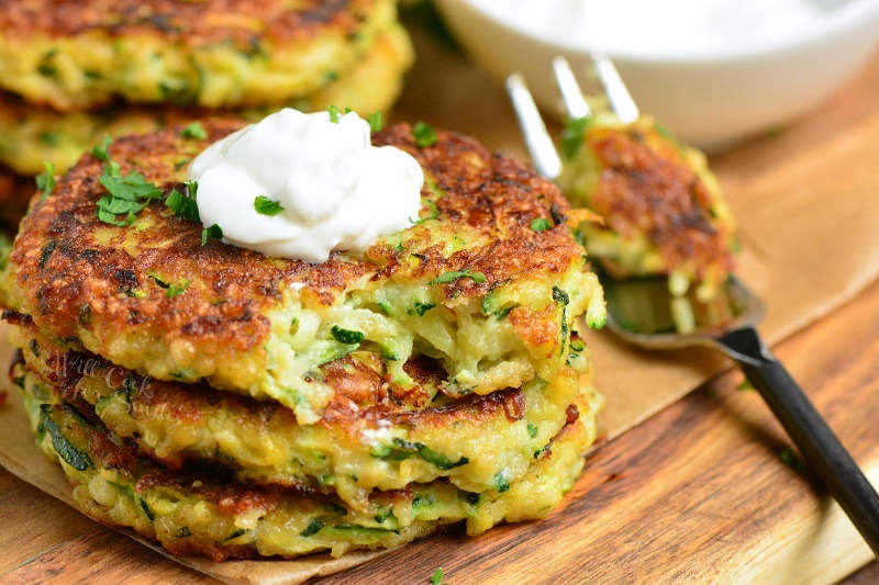 zucchini fritters on a wood cutting board with sour cream on top and a fork 