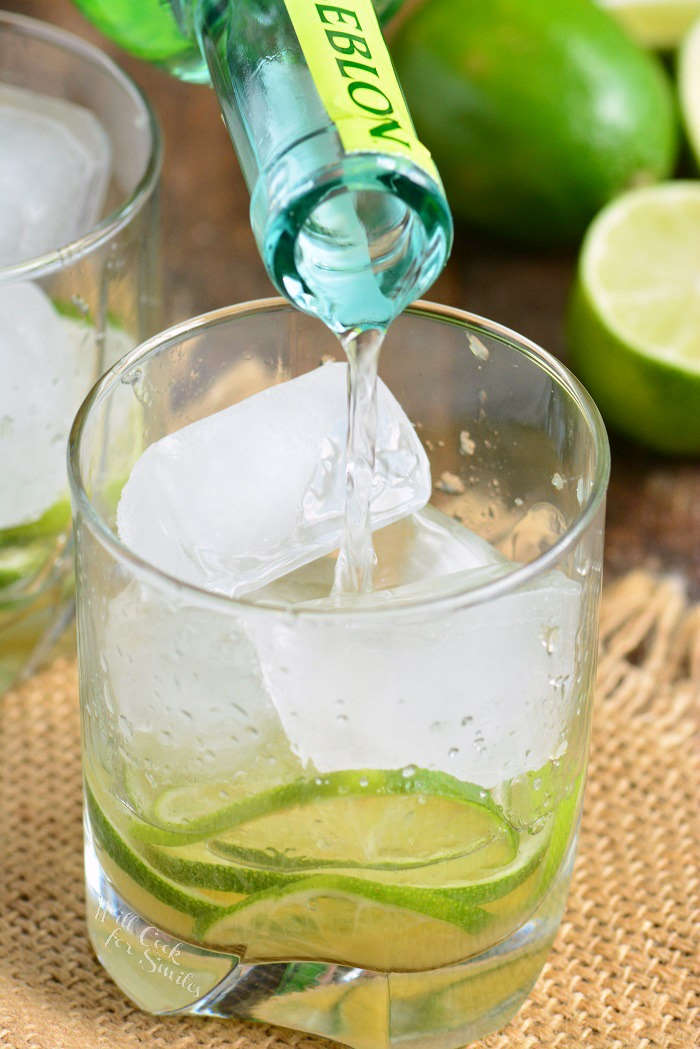 pouring a caipirinha into a glass with limes 