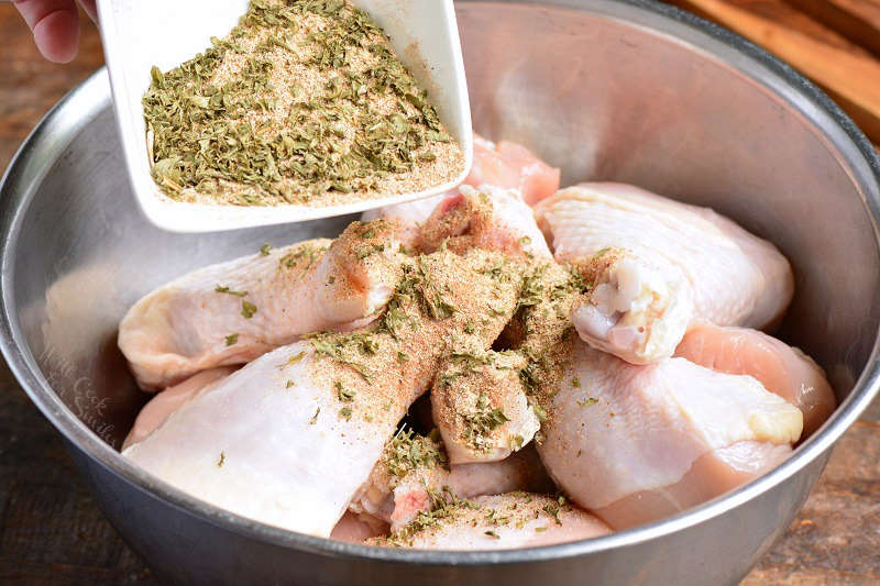 pouring the chicken seasoning out if small bowl onto the chicken drum sticks in a metal bowl 