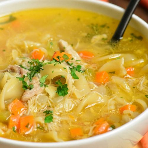 chicken soup in a white bowl with a spoon to the right 