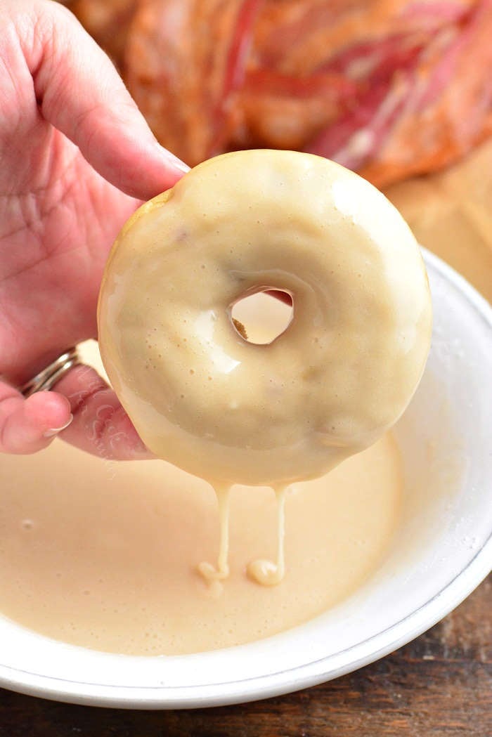 glazed donut being pulled out of a bowl of glaze