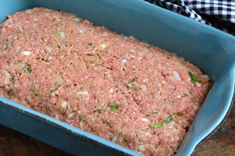meatloaf mixture spread in the blue baking loaf pan.