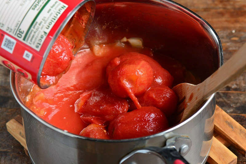 pouring whole tomatoes out of a can into the cooking pot