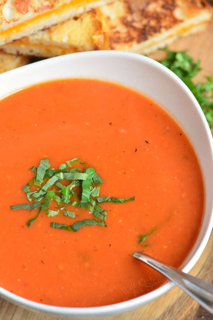 closeup view of tomato soup in a white bowl topped with fresh basil and spoon in a bowl