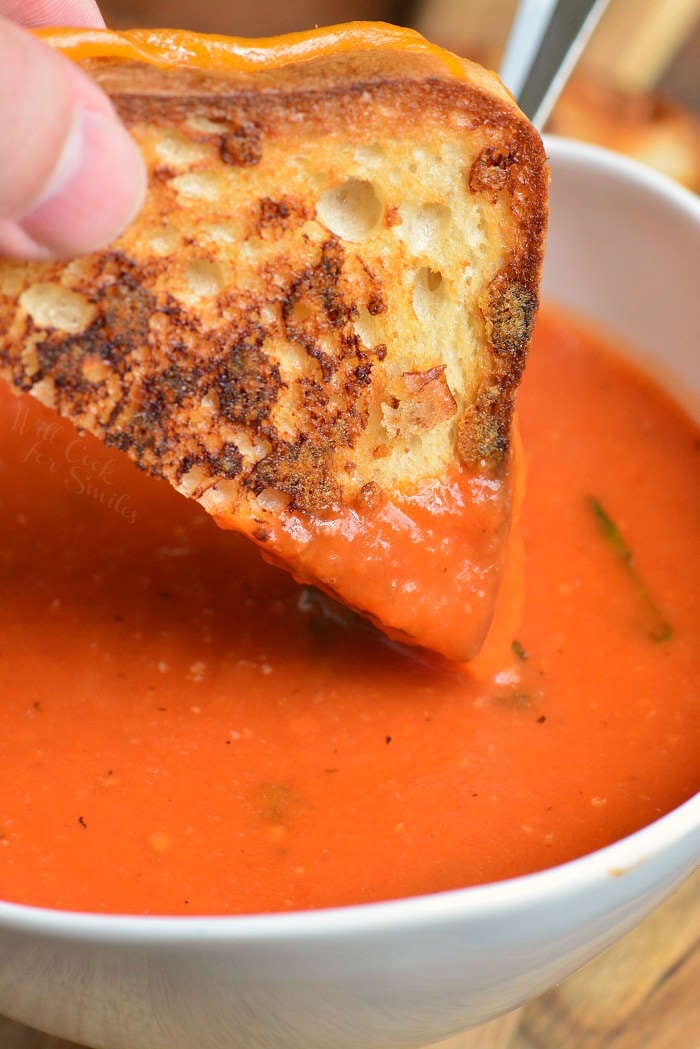 dipping a grilled cheese triangle half into the bowl of tomato basil soup
