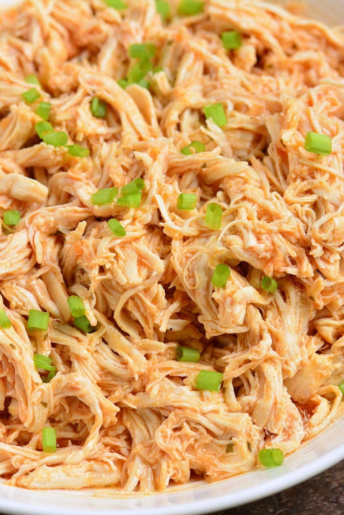 shredded buffalo ranch chicken in a bowl topped with green onions.