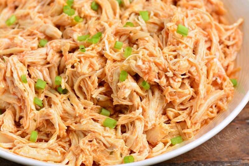 buffalo shredded chicken in a bowl with diced green onions on top 
