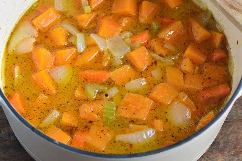 vegetables covered in chicken stock cooking in the white pot.