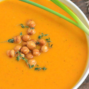 a white bowl full of butternut squash soup with a scallion on top and chickpeas.