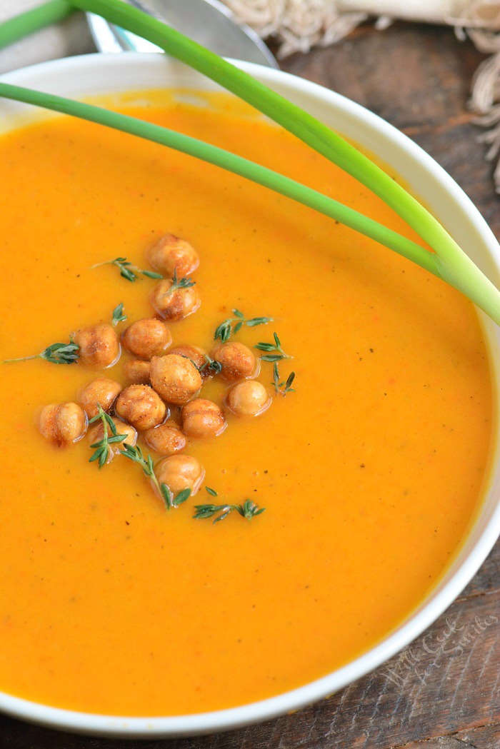 a white bowl full of butternut squash soup with a scallion on top and chickpeas.