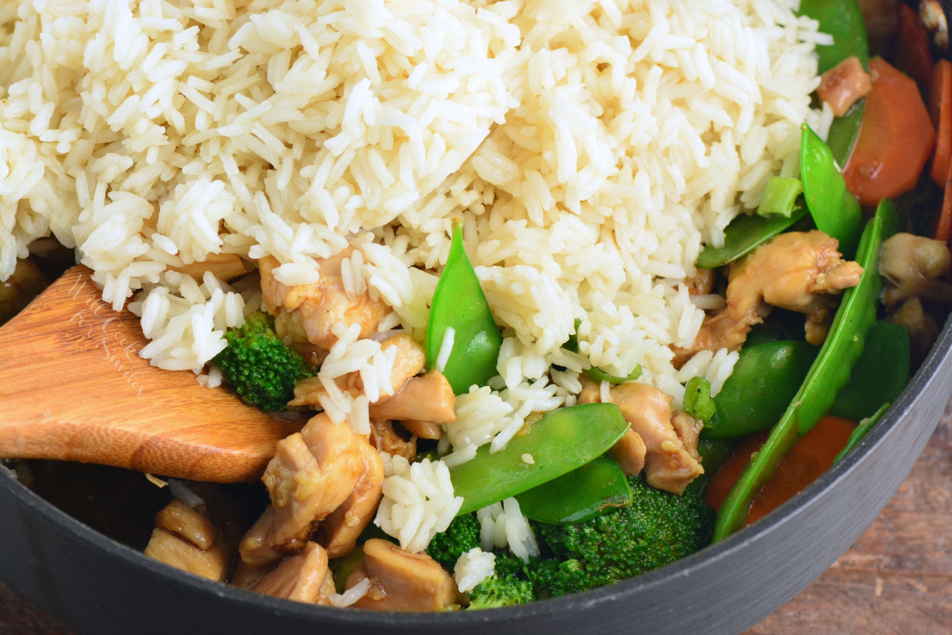 adding rice to the chicken teriyaki and vegetables to the rice bowl.
