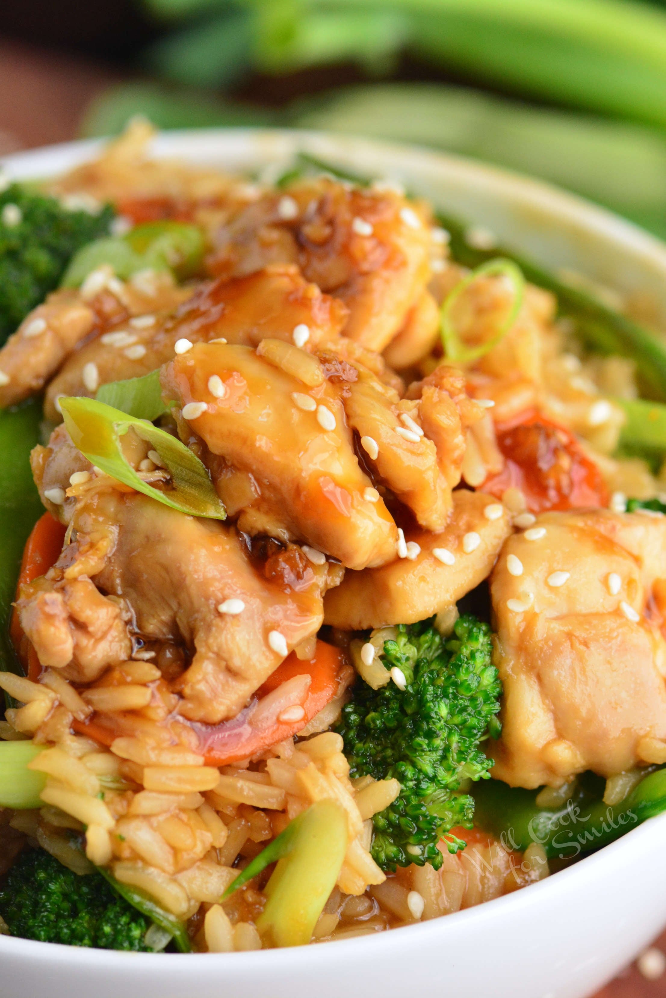 chicken teriyaki mixed with vegetables and rice in a bowl topped with sesame.