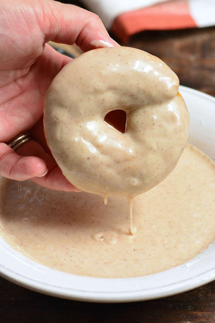 dipping pumpkin donuts in glaze that is in a bowl 