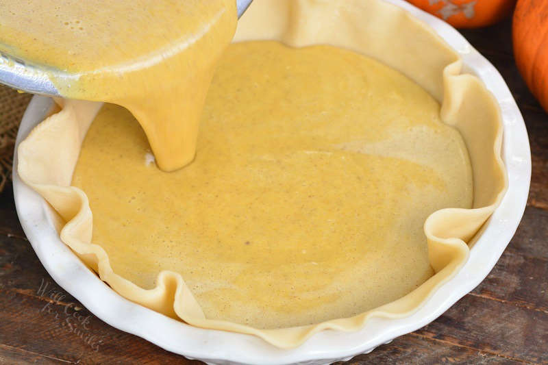 pouring in pumpkin pie batter into the crust in a dish.