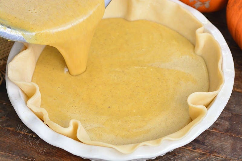 pouring in pumpkin pie batter into the crust in a dish.