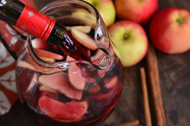 pouring red wine into the pitcher on a wood cutting board with apples and cinnamon 