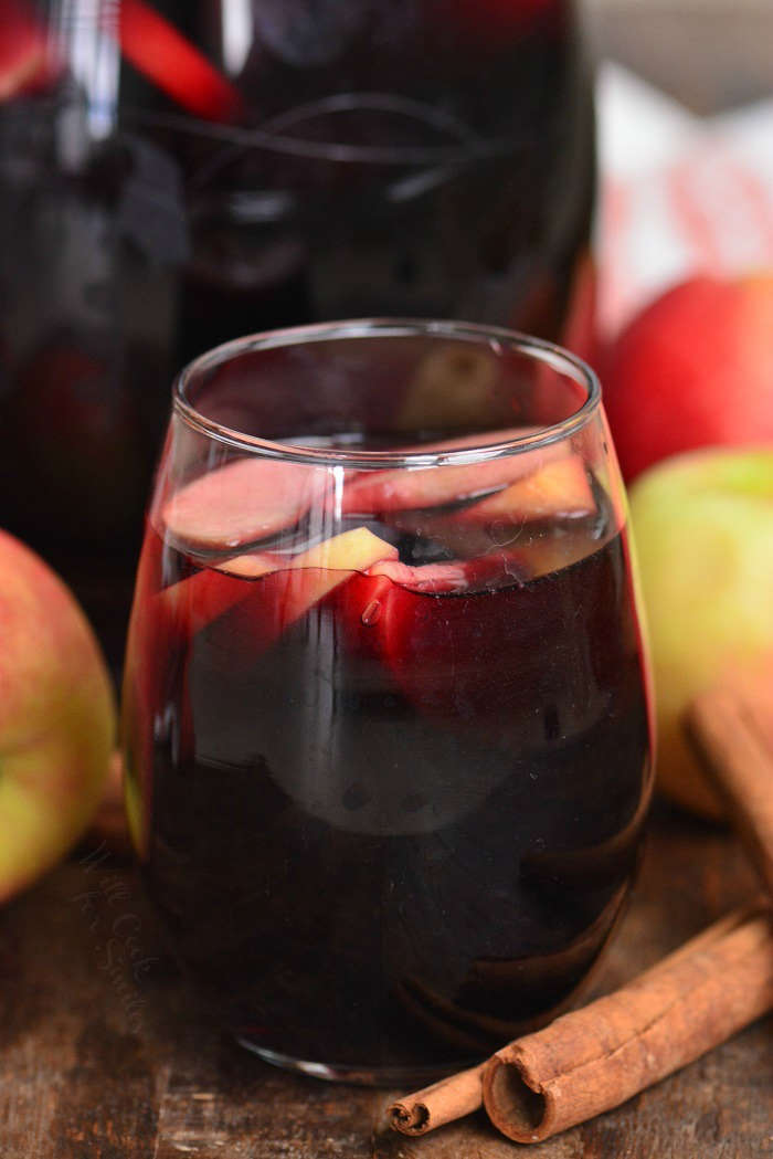 apple sangria in a wine glass on a wood table with apples and cinnamon sticks 