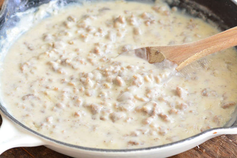 stirring cooked sausage gravy in a skillet with a spoon