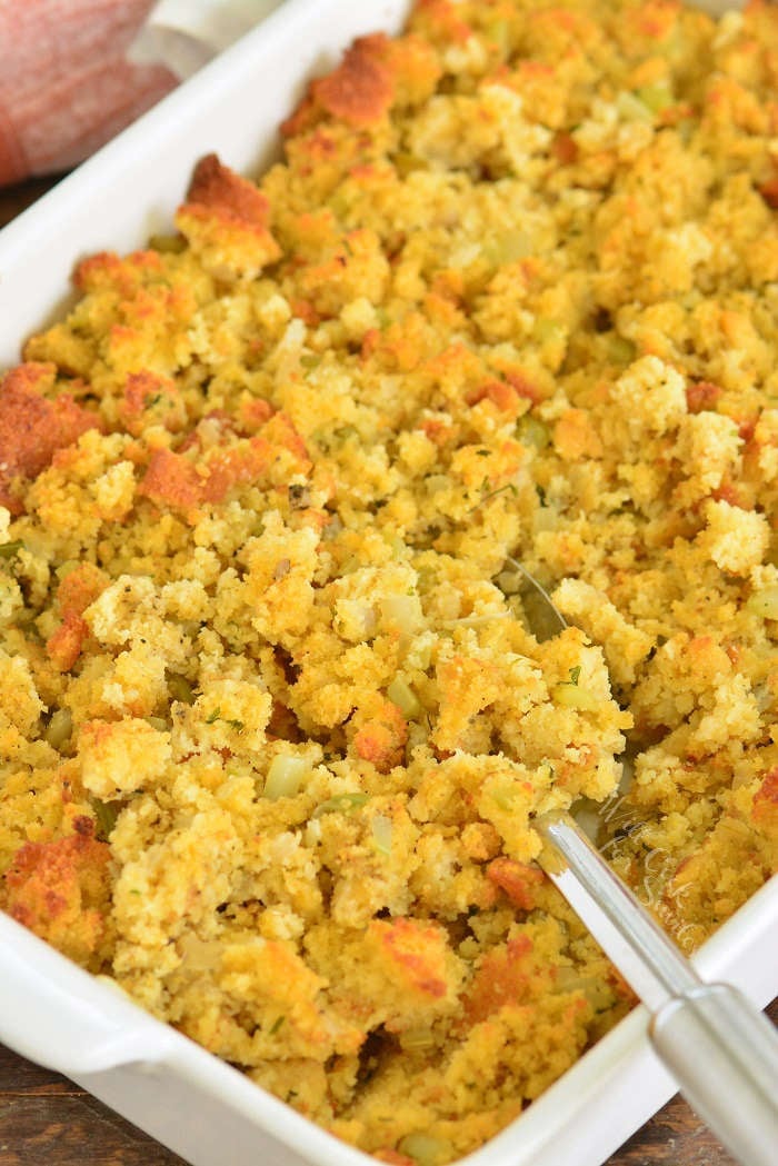 spooning cornbread dressing in a baking pan with a spoon scooping some out 